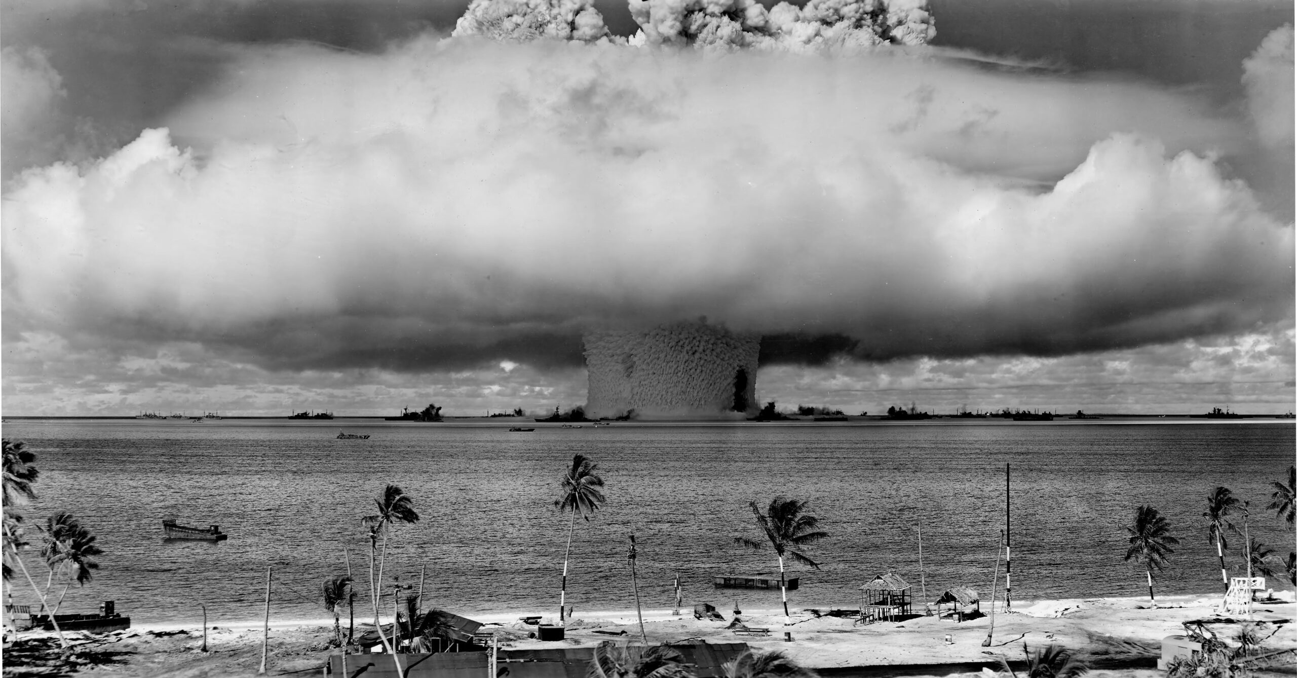 Sort-hvidt fotografi af atomprøvesprængningen Operation Crossroads Baker ved Bikini-atollen i 1946, med en massiv vandsøjle og skysvamp set fra stranden