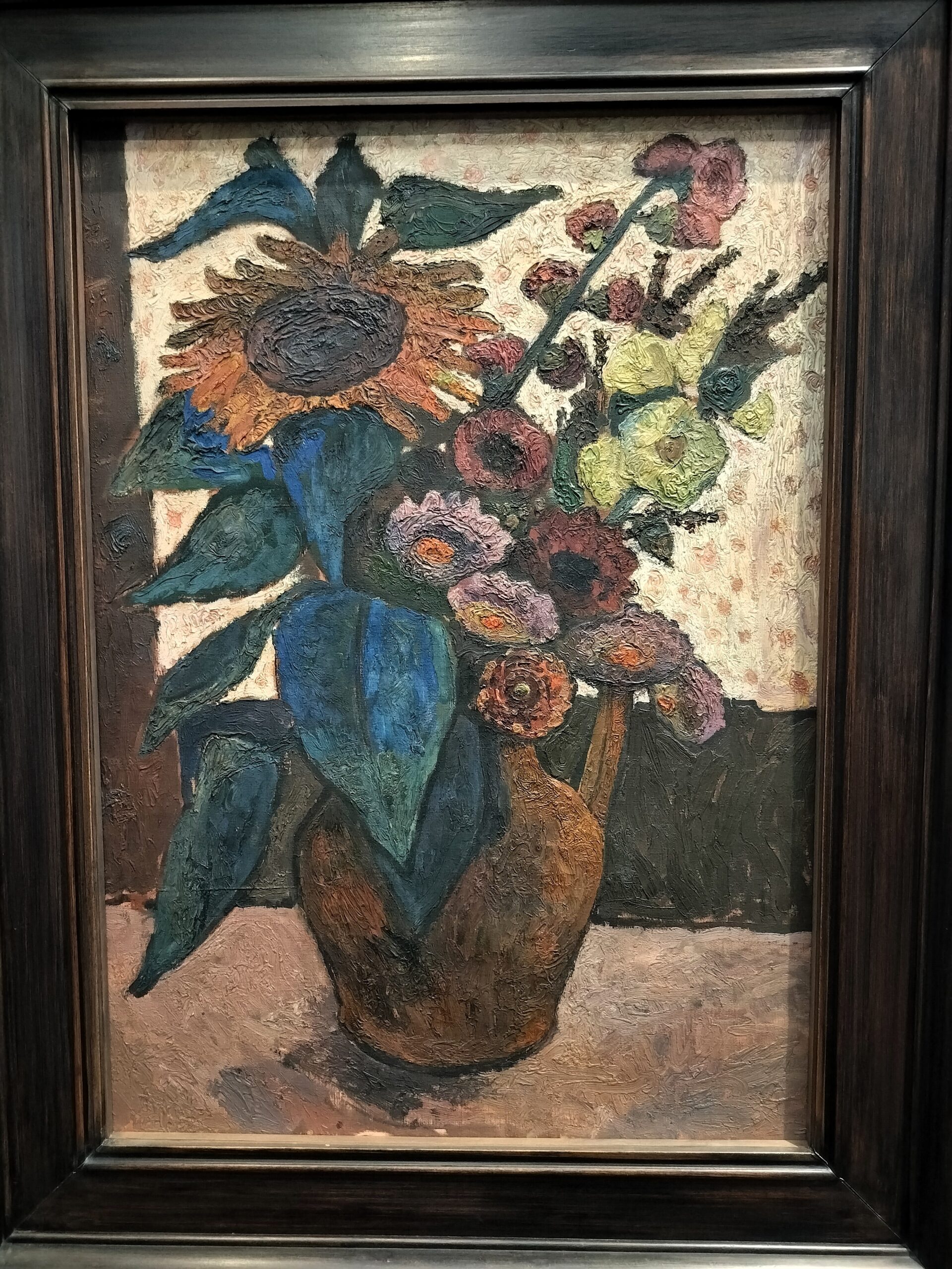 Paula Modersohn-Beckers maleri Stilleben med en solsikke, stokroser og georginer (1907): en stor solsikke, lyserøde og gule stokroser og røde og violette georginer med blågrønne blade i en brun kande. Malingen er lagt tykt på foran en lys, mønstret baggrund.